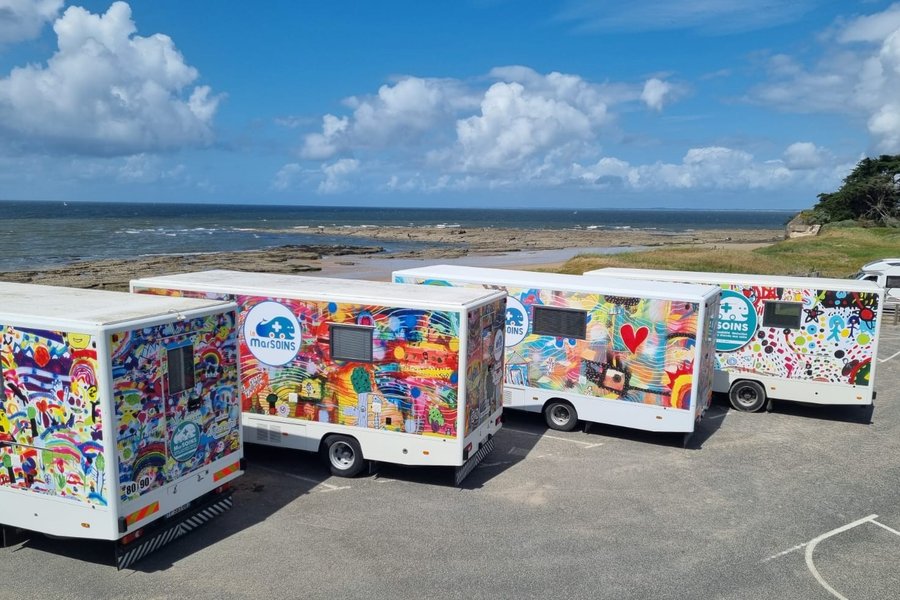Quatre camions MarSOINS aux couleurs de dessins d'enfants, garés côte à côte face à la mer.